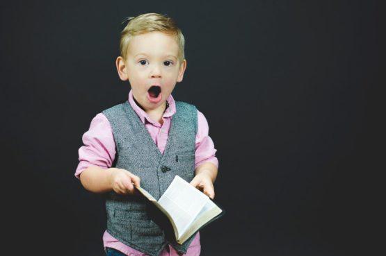 little boy in suit vest with shocked expression while holding book